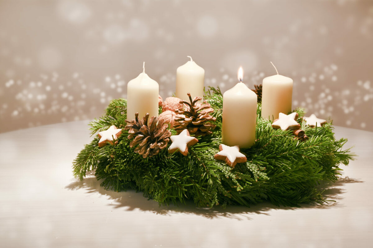 First Advent – decorated Advent wreath from fir and evergreen branches with white burning candles, tradition in the time before Christmas, warm background with festive bokeh and copy space, selected focus